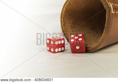 Red Dices With Dice Cup On A White Wooden Table.