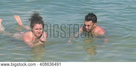 Young Beautiful Woman And Man Lying In Water In Sea While Sunbathing. Couple Of Tourists Are Bathing