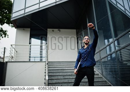 Middle Eastern Entrepreneur Wear Blue Shirt, Eyeglasses With Laptop Against Office Building.
