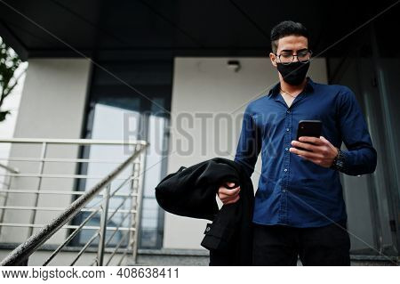 Middle Eastern Entrepreneur Wear Black Face Mask And Eyeglasses Look At Mobile Phone. New Normal Lif