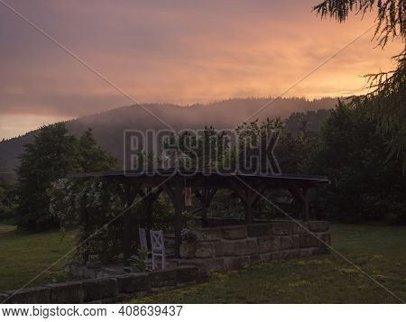 View Of Summer Garden With Tiber Wooden Gazebo Pergola With Blooming Climbing Plant Flowers And Whit
