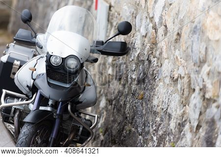 Off-road Motorcycle At The Stone Wall. A Gray Motorcycle Is Leaning Against The Wall.