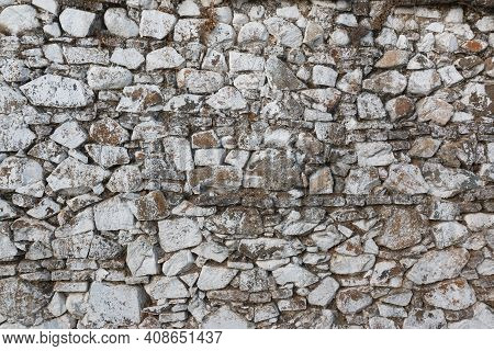 Old Stone Wall, Painted In A Faded White Color And Built With Stones And Mud