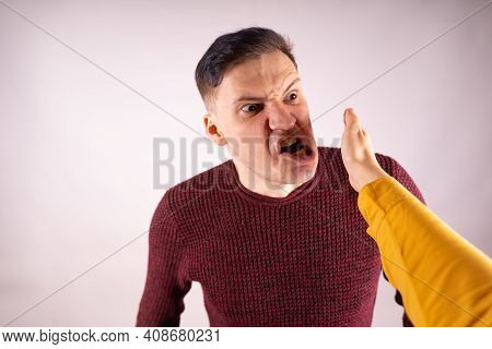 Crop Person Slapping Scared Man In Face. Emotional Male Getting Slapped In Face While Shouting With
