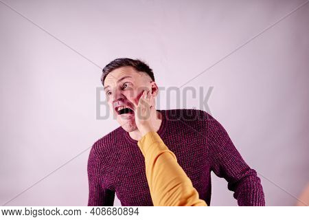 Crop Person Slapping Scared Man In Face. Emotional Male Getting Slapped In Face While Shouting With