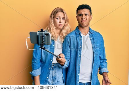 Young interracial couple taking a selfie photo with smartphone clueless and confused expression. doubt concept. 