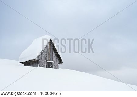 Winter snowy landscape with wooden snow covered cabin on a hill
