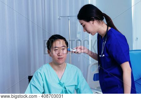 Young Female Medical Worker With Stethoscope Examining Ears Of Asian Male Patient In Uniform Using T