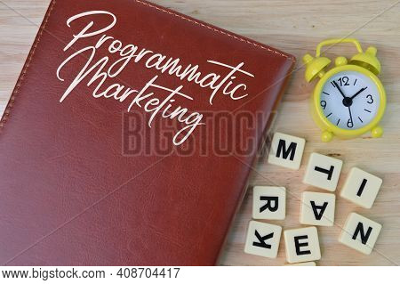 Top View Of Clock, Square Letters And Notebook Written With Programmatic Marketing.