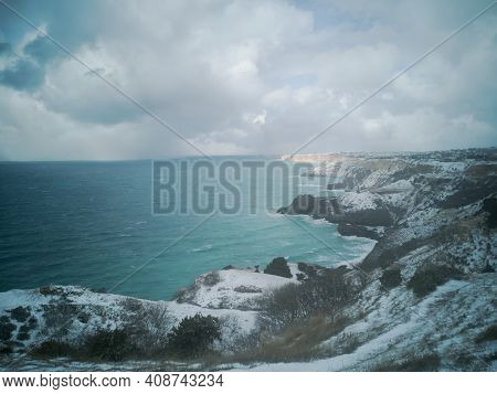 A Snow Storm Covered The Seashore. Bright Turquoise Sea, Squally Wind, Huge Waves, Cloudy Sky. The C