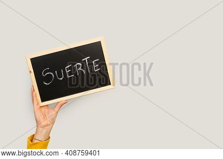Woman Holding A Blackboard With Suerte Word On A Gray Background (luck)