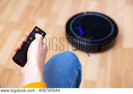 Man Resting While Robotic Vacuum Cleaner Doing Chores, Clean Work At Home. Man Controls A Robot Vacu
