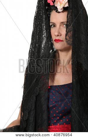 Uma mulher vestindo uma mantilla, um vestido de espanhola e flores na cabeça.