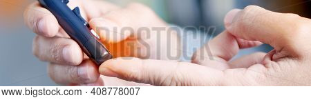 closeup of a young caucasian man about to measure his blood glucose level in a glucose meter by pricking his finger with a fingerstick, in a panoramic format to use as web banner or header