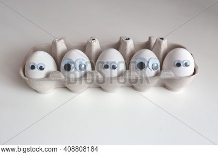 Eggs With Eyes. A Box With White Eggs On A White Table.