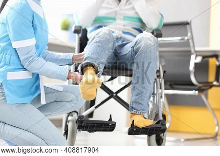 Rehabilitation Doctor Helping To Lift Leg Of Patient In Wheelchair Closeup. Recovery From Injuries C