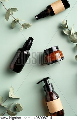 Amber Glass Cosmetic Bottles And Eucalyptus Leavers On Green Background Top View. Spa Natural Organi