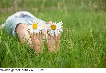 Child With Daisy Lying In Sunny Meadow And Relaxing In Summer Sunshine. Boy Lying On Green Grass Out