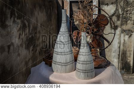 Dried Flowers In Two Ceramic Vase On Pink Textured Table Cloth And Vintage Fan With Old Cement Wall.