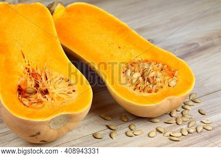 Pumpkin Butternut Liscia Cut In Half. Yellow Delicious Pumpkin On Wooden Table, Seeds Around.