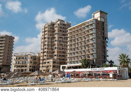 Famagusta, Cyprus - September 15 2016: Palm Beach With Beach Umbrellas And Tourists And The Abandone