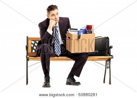 Disappointed redundant businessman in a suit sitting on a bench with a box of belongings isolated on white background