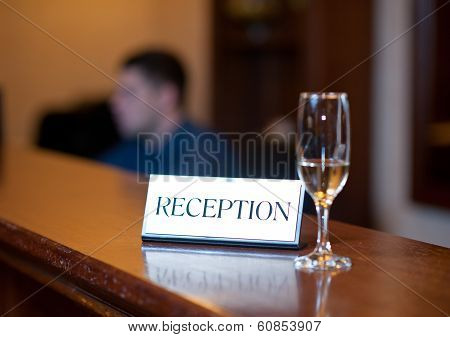 Reception card and champagne glass isolated on wooden table. Reception desk with card and glass
