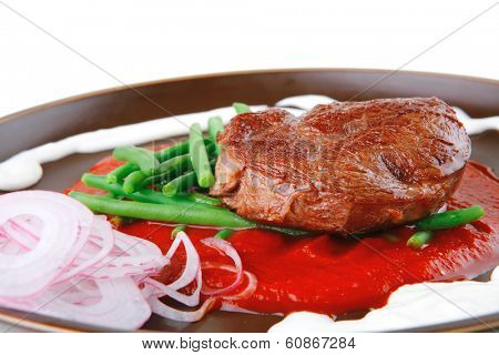 pork medallion served on tomato sauce with green peas on dark plate isolated on white background