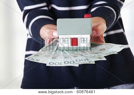 Woman holding PLN ( polish zloty ) bills and house model over white - real estate loan concept