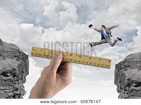 Young businessman in suit jumping over mountain gap