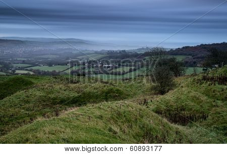 Beautiful Sunrise Dawn Landscape Of Hills Overlooking Brightly Lit Town In Valley Below