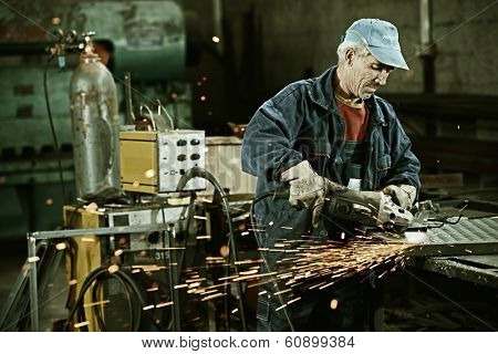 Industrial worker cutting and welding metal with many sharp sparks
