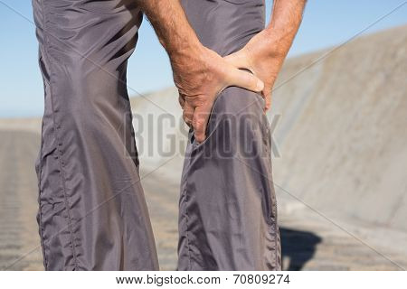 Active senior man touching his injured knee on a sunny day