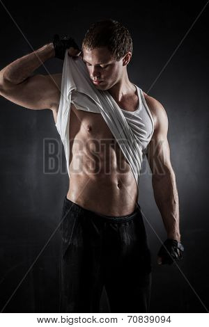 Brutal athletic man taking shirt off on gray background