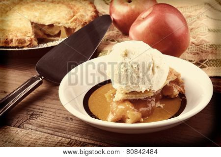 Closeup of a slice of Apple Pie a la Mode. Fresh Fuji apples and a whole pie are in the background. Horizontal format with instagram effect applied.