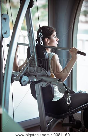 Woman weight training at gym.Exercising on pull down weight machine.Woman doing pull-ups exercising