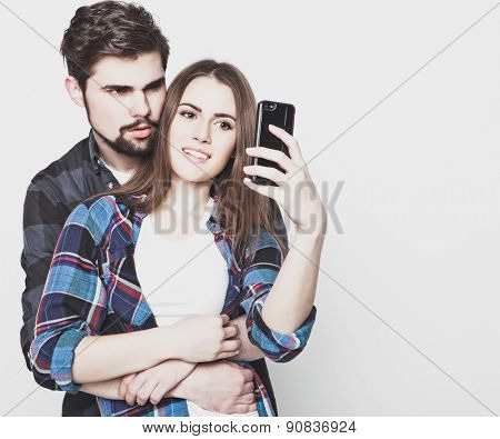 tehnology, internet, emotional  and people concept: Capturing happy moments together. Happy young loving couple making selfie and smiling while standing against white background.