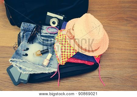 Open the suitcase with tourist things: women's hat, swimsuit, camera, denim shorts, dresses, sunglas