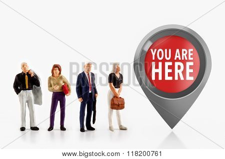 miniature people  - people stand in front the sign you are here