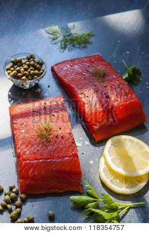 Two pieces of raw wild salmon fish steaks with lemon, capers and herbs, ready to cook