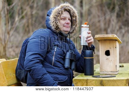 Ornithologist drinking tea in park near wooden bird cage