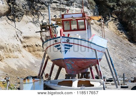 A small fishing boat out of the water, for repairs, in Vlychada village, Santorini island, Greece