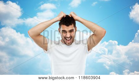 emotions, stress, madness and people concept - crazy shouting man rending ones hair in t-shirt over blue sky and clouds background