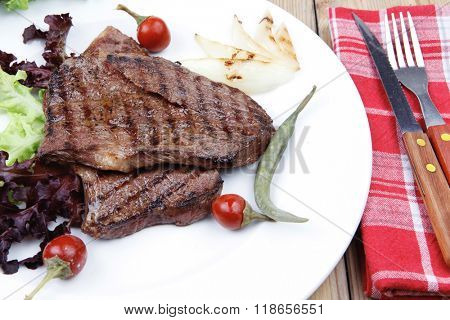 meat food : roast steak boneless with roast onion and red hot peppers, served on green lettuce salad on dish isolated over wooden table