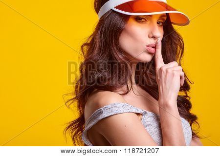 Smiling young woman in orange  sun visor posing in sunlight and looking away. studio shot on yellow background.