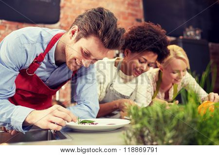cooking class, friendship, food and people concept - happy women cooking and decorating plates with dishes in kitchen