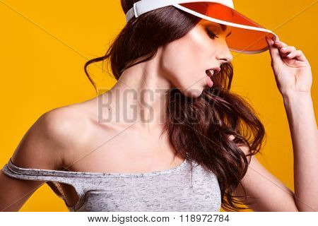 Smiling young woman in orange  sun visor posing in sunlight and looking away. studio shot on yellow background.