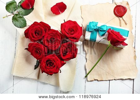 Fresh red roses buds in shape of heart with linen fabric and present box on wooden background