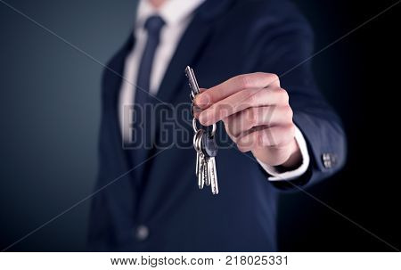 Young businessman hand over keys with empty dark background
