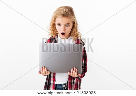 Portrait of an astonished little girl looking at laptop computer screen isolated over white background